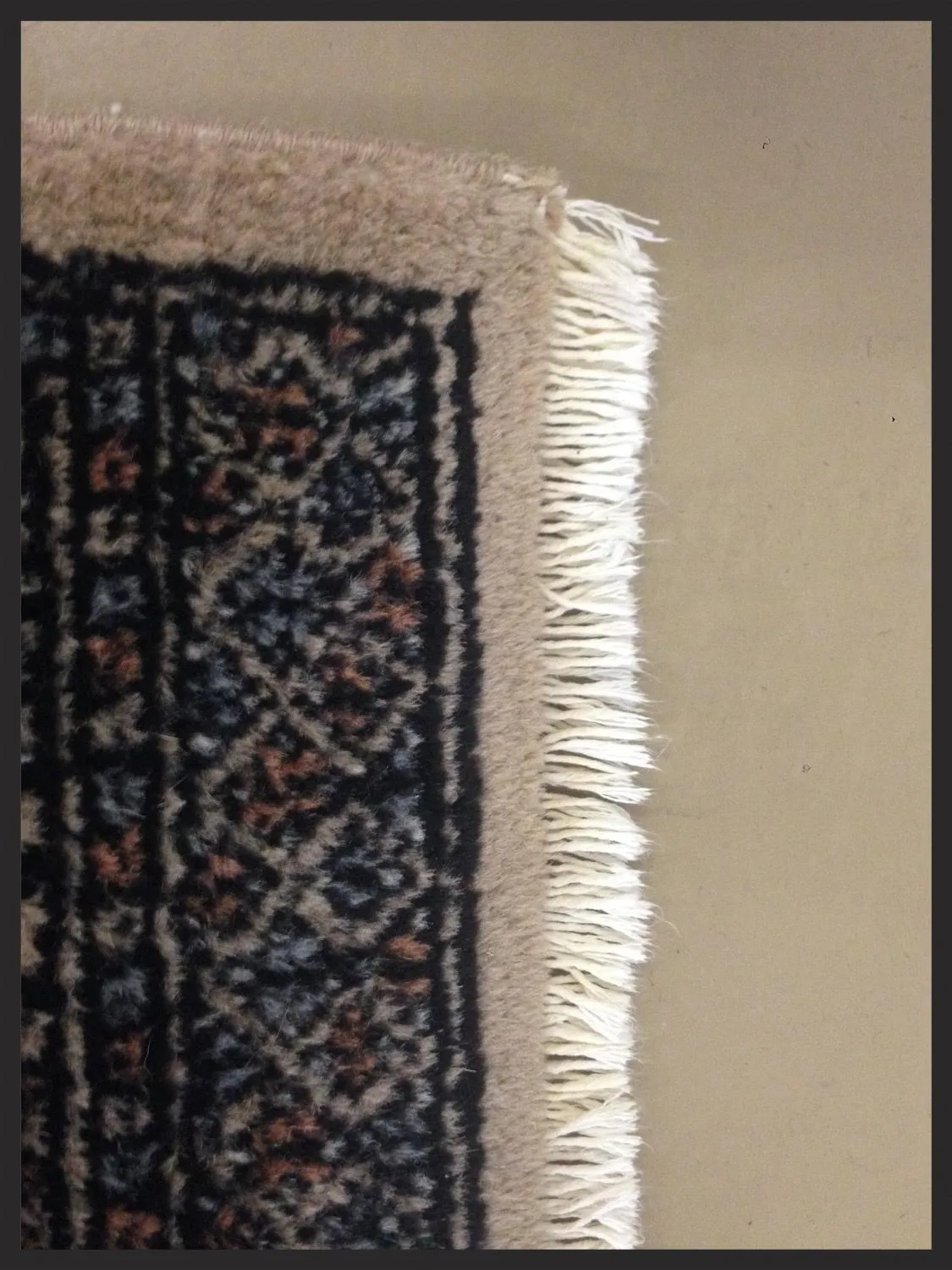 Corner of a wool rug with worn fringe before overcasting repair