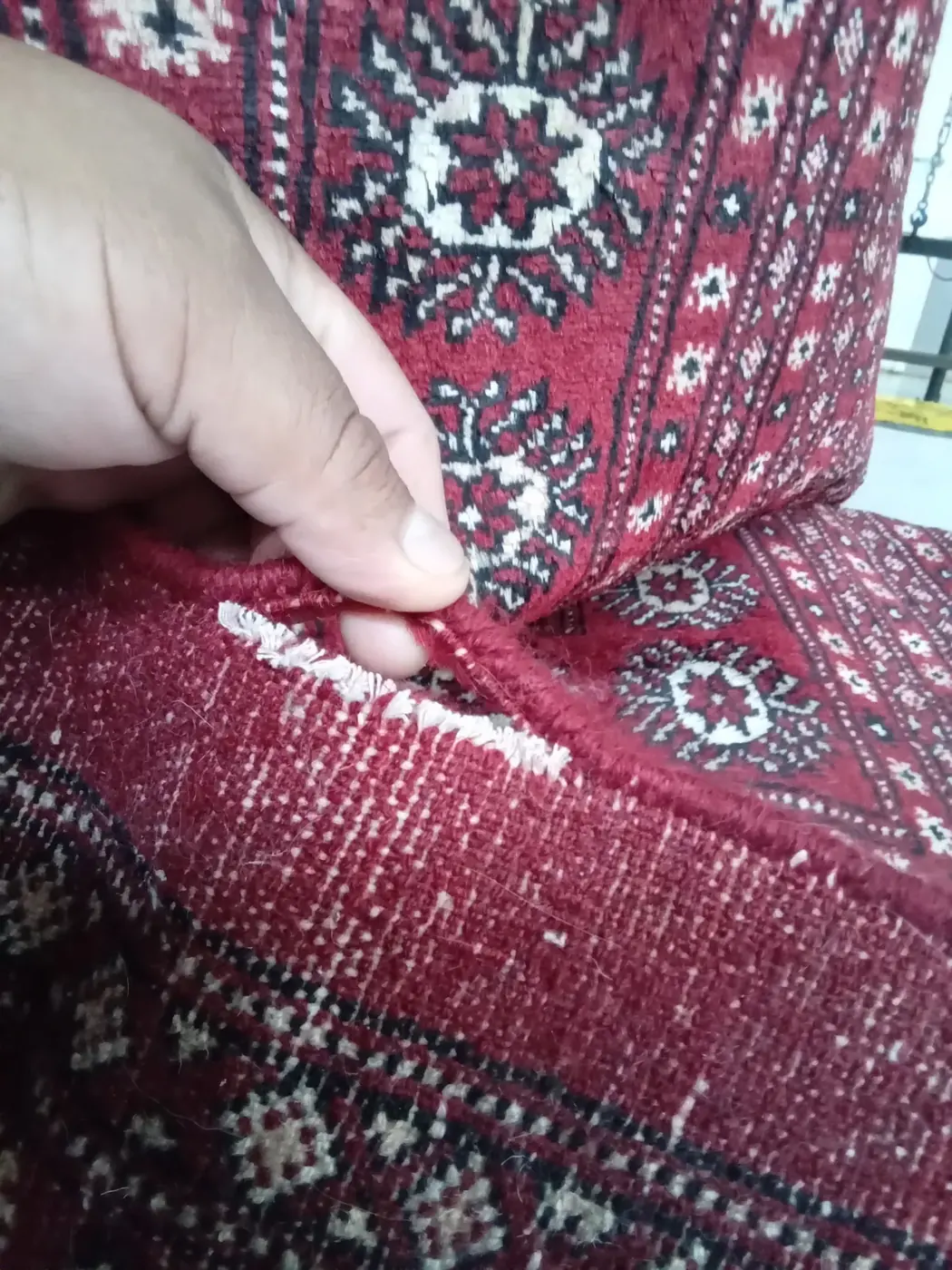 Hand at a worn area on a red Bokhara rug